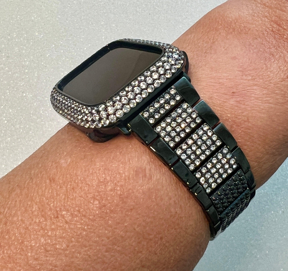 A black watch with a diamond-encrusted bezel and bracelet is worn on a person's wrist.