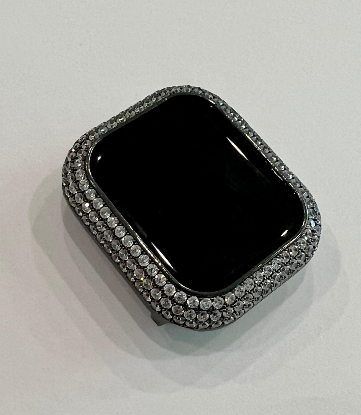 A black square-shaped object with a sparkling, diamond-encrusted frame around it, sitting on a white surface.