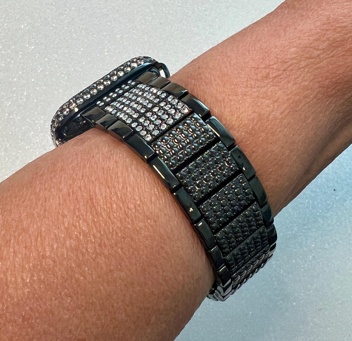 A close-up view of a person's wrist wearing a black watch with a metallic band adorned with small diamonds.