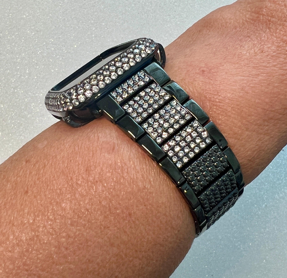 A close-up view of a person's wrist wearing a black watch with a diamond-encrusted band.