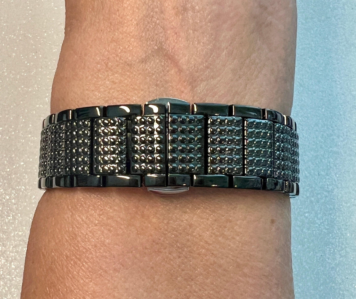 A close-up view of a person's wrist wearing a black metal watch with a textured band.